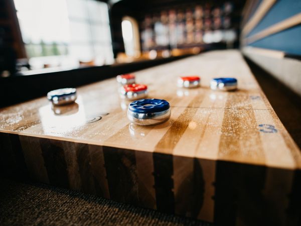 Close-up of shuffleboard pucks on a wooden shuffleboard table in a room with blurred background.