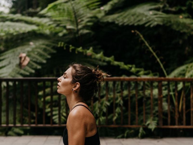 Woman practicing yoga outdoors in upward dog pose, surrounded by lush green plants and trees.