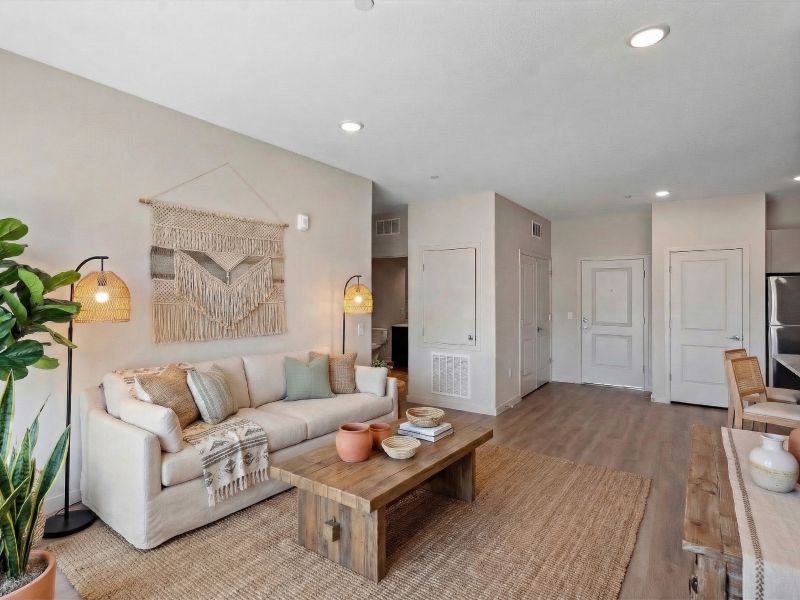 Neutral-toned living room with a beige sofa, wooden tables, plants, and woven decor on the wall.
