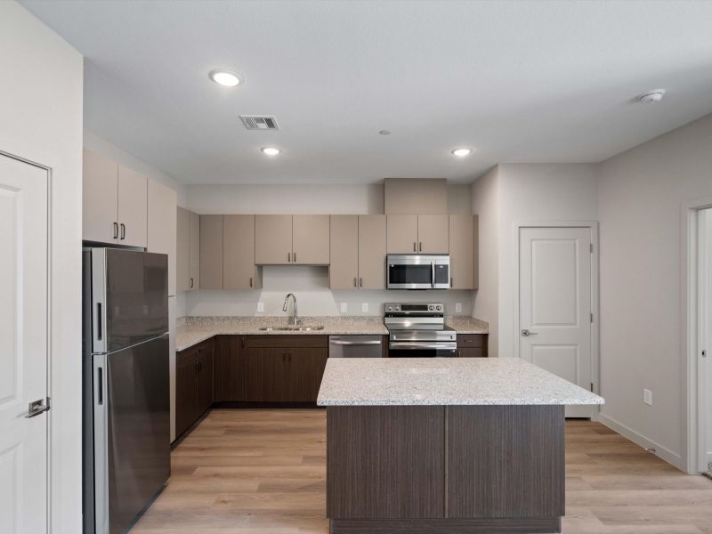 Modern kitchen with stainless steel appliances, an island, light cabinets, and wood flooring.