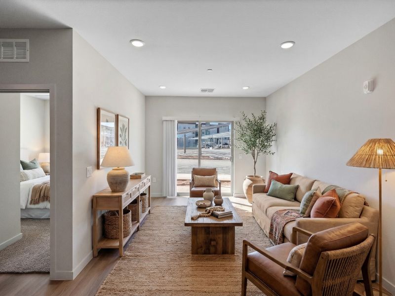 Bright living room with neutral decor, wooden furniture, and large window beside a bedroom entry.