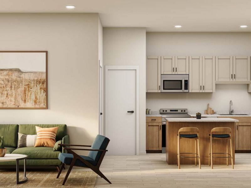 Modern living room with green sofa, armchair, and open kitchen with island and barstools under bright lighting.