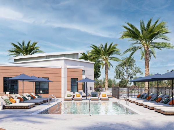 Outdoor swimming pool with lounge chairs, umbrellas, palm trees, and modern buildings under a blue sky.